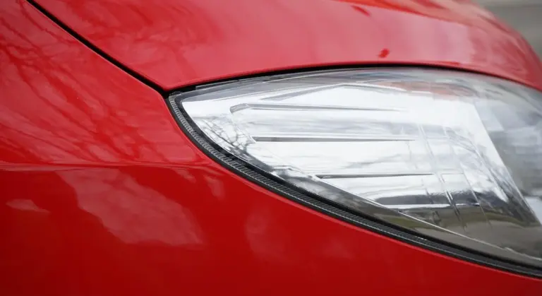 Close-up of a red car showing glossy paint near the headlight.