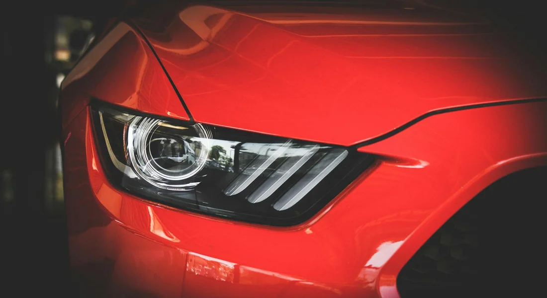 Close-up of a glossy red car front panel and headlight, illustrating the painted surface after spraying.