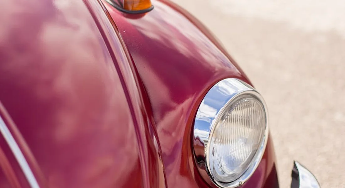 Close-up of a glossy red vintage car headlight and body panel.