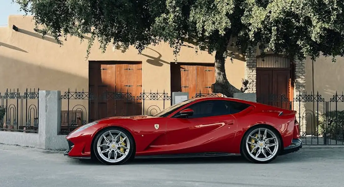 Red Ferrari sports car with a vinyl wrap, parked on a city street with a tree and beige building in the background.