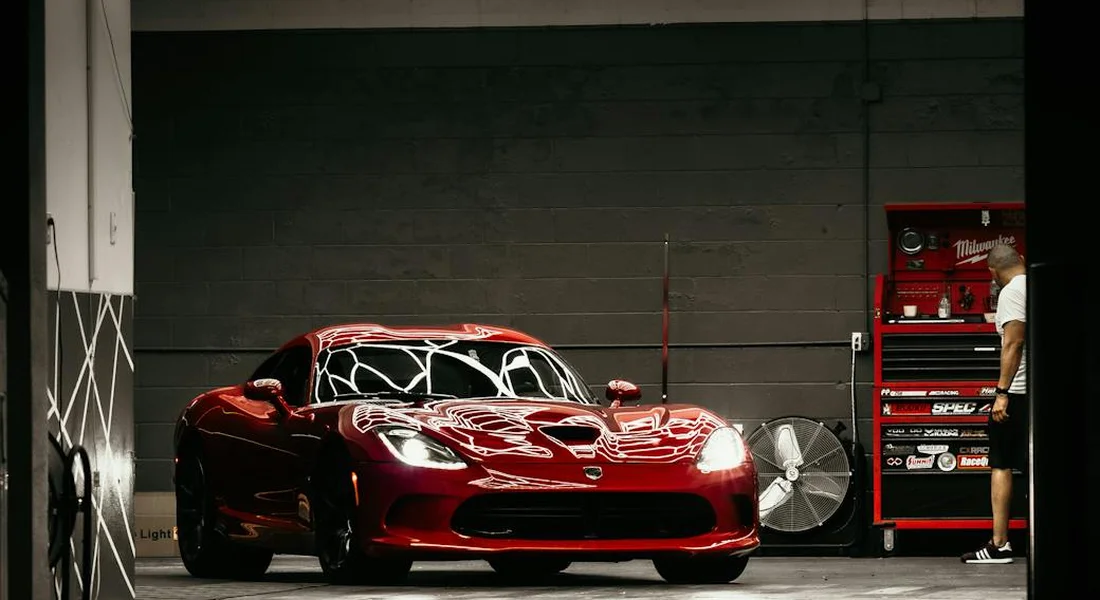 Red sports car in a garage with a technician near a red toolbox, emphasizing careful paint care and scratch prevention.