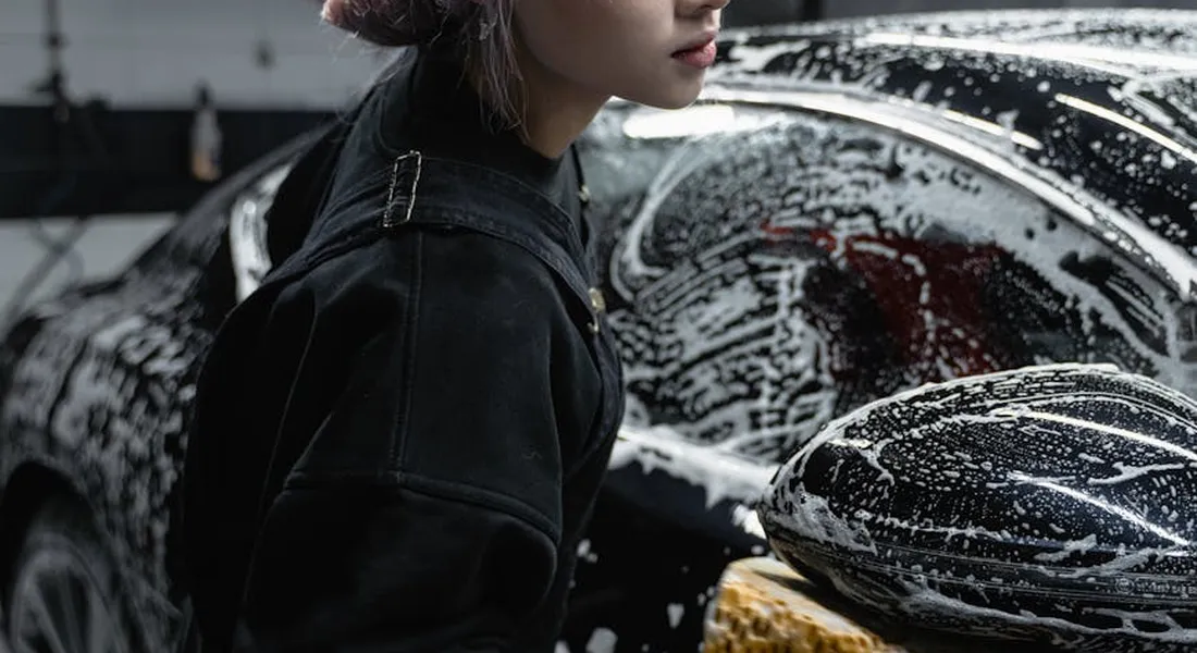 Person washing a car with soap suds on the hood, illustrating cleaning before returning a rental vehicle.