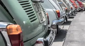 Row of vintage cars parked along a street, showing colorful rear ends and tail lights.