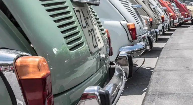 Row of vintage cars parked along a street, showing colorful rear ends and tail lights.