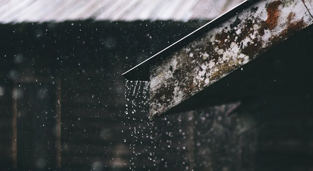 Close-up of a rusted metal edge with droplets of water, highlighting corrosion spots on a car’s body.