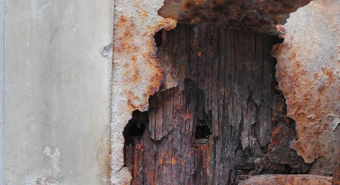Close-up of a rusted, peeling metal surface with dark, exposed substrate, illustrating substrate condition for chemical paint stripping.