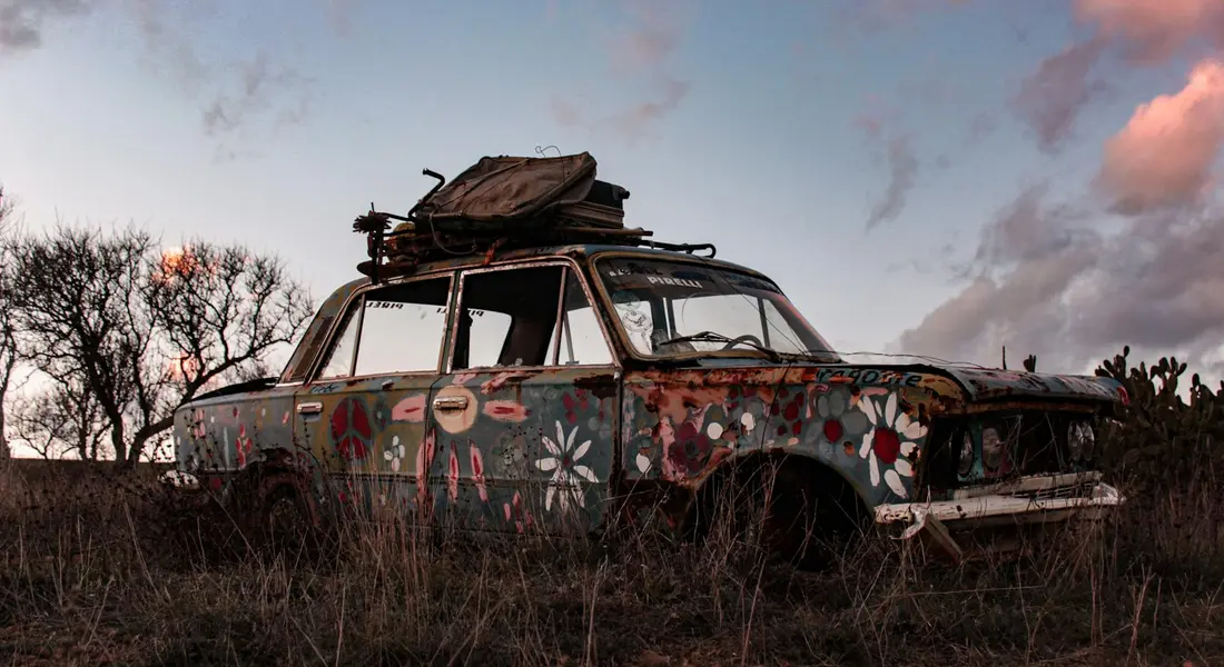 Old rusted car with decorative flowers painted on it sits in a field at sunset, illustrating how improper rust removal can damage existing paint.