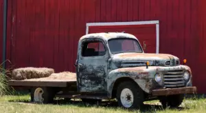 Rusty vintage pickup on a trailer in front of a red barn, illustrating corrosion