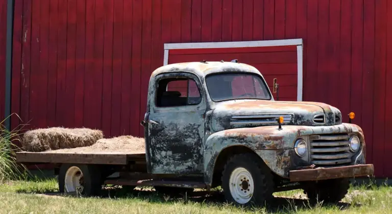 Rusty vintage pickup on a trailer in front of a red barn, illustrating corrosion