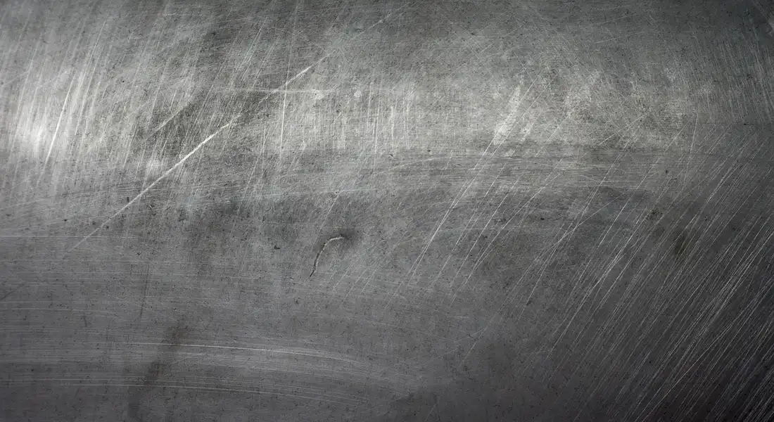 Close-up of a metal surface with multiple superficial scratches, illustrating surface damage to be treated with scratch removers.