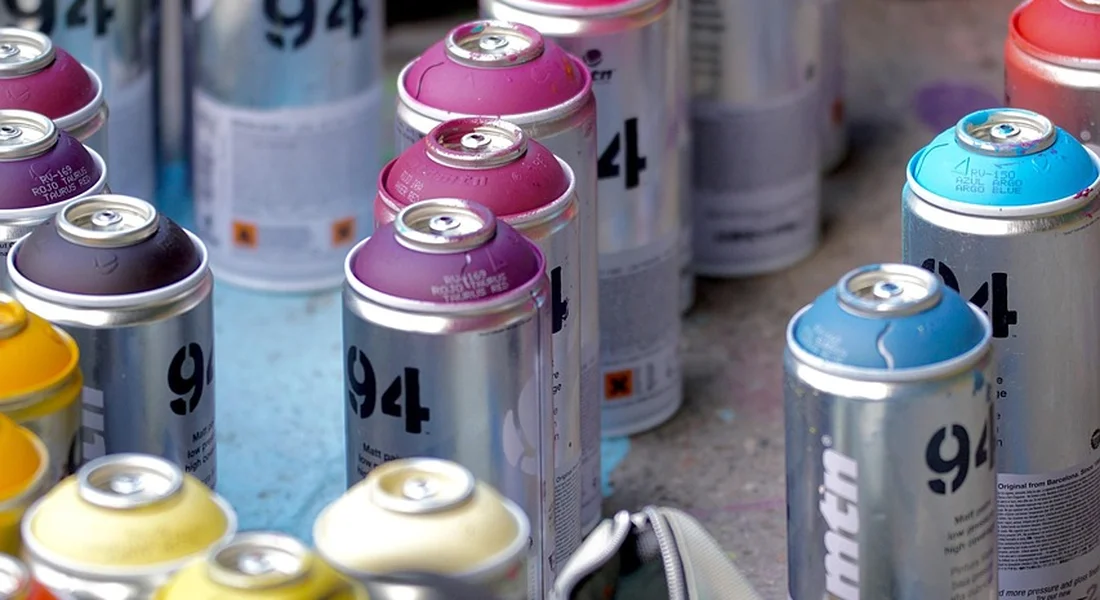 Assorted spray paint cans with colorful caps arranged on a work surface, illustrating nozzle size considerations for car painting