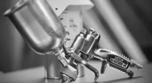 A close-up, grayscale photo of an automotive spray gun used for applying paint.