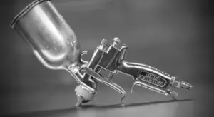 Close-up of a metal spray paint gun with a paint cup in grayscale