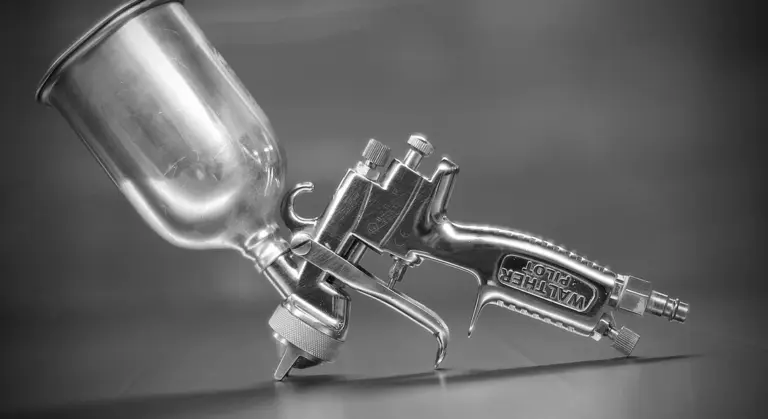 Close-up of a metal spray paint gun with a paint cup in grayscale