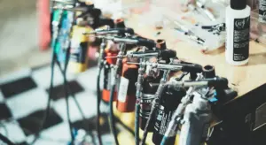 Row of spray guns hanging on a rack above a wooden workbench, with a bottle of solvent visible in the background.