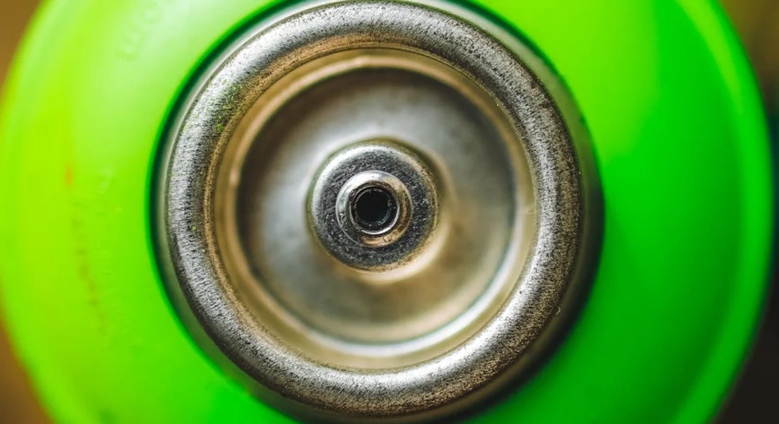 Close-up of a spray paint nozzle surrounded by a bright green can.