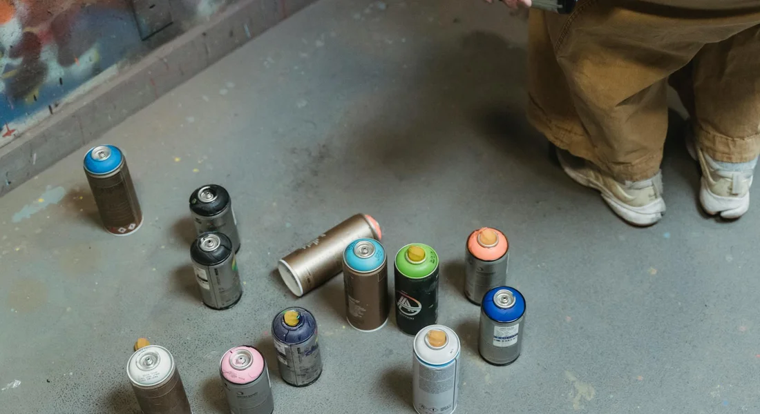 Assorted spray paint cans on a workshop floor with a person standing nearby, illustrating a DIY car spray-paint setup