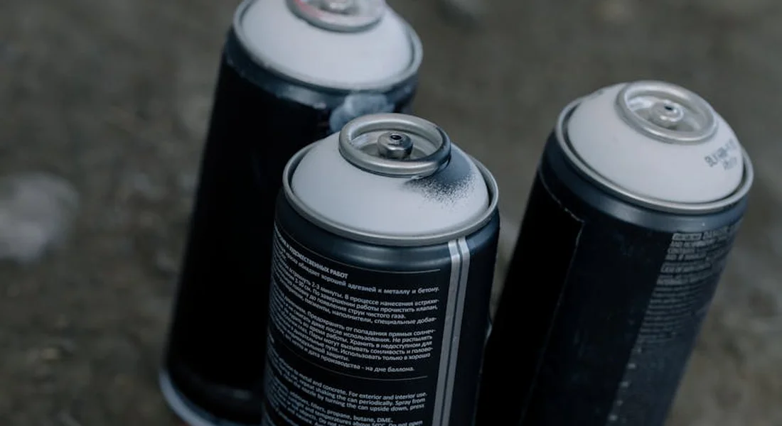 Three spray paint cans standing upright on a work surface with a blurred background.
