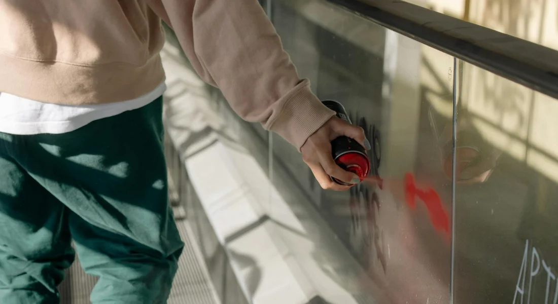 Person using red spray paint near a car's exterior, illustrating the risk of paint damage from spray splatter.