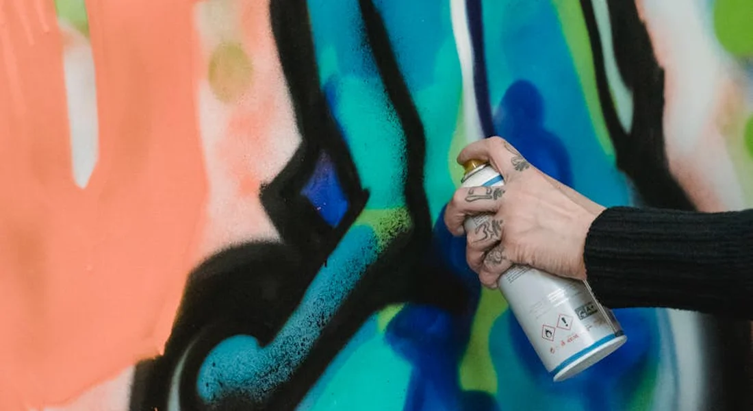 Close-up of a hand holding a spray paint can and spraying colorful graffiti on a wall.