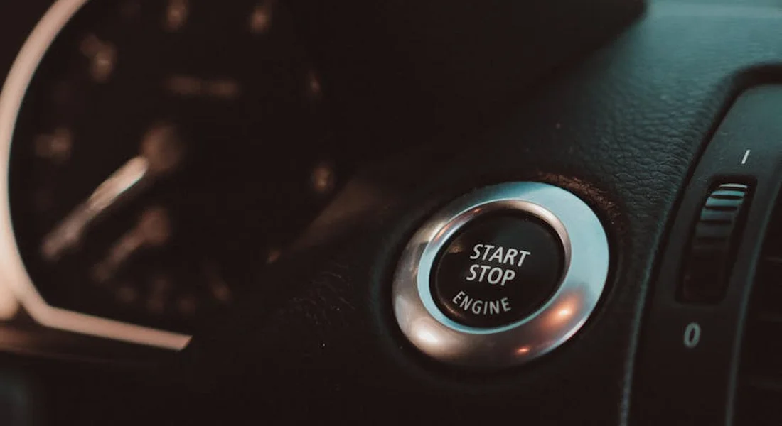 Close-up of a car's Start/Stop engine button on the dashboard inside a dark vehicle interior.