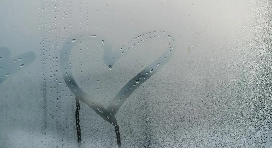 A heart drawn on a foggy car window with condensation droplets.