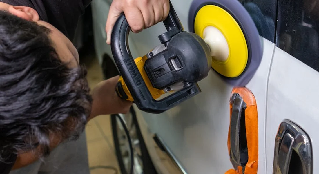 Person using a handheld polisher on a car door panel with a yellow polishing pad, buffing the area near the door handle.