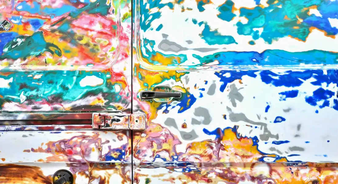 Close-up of a car door covered in vibrant splashes of paint, illustrating the importance of checking common locations for the paint color code.