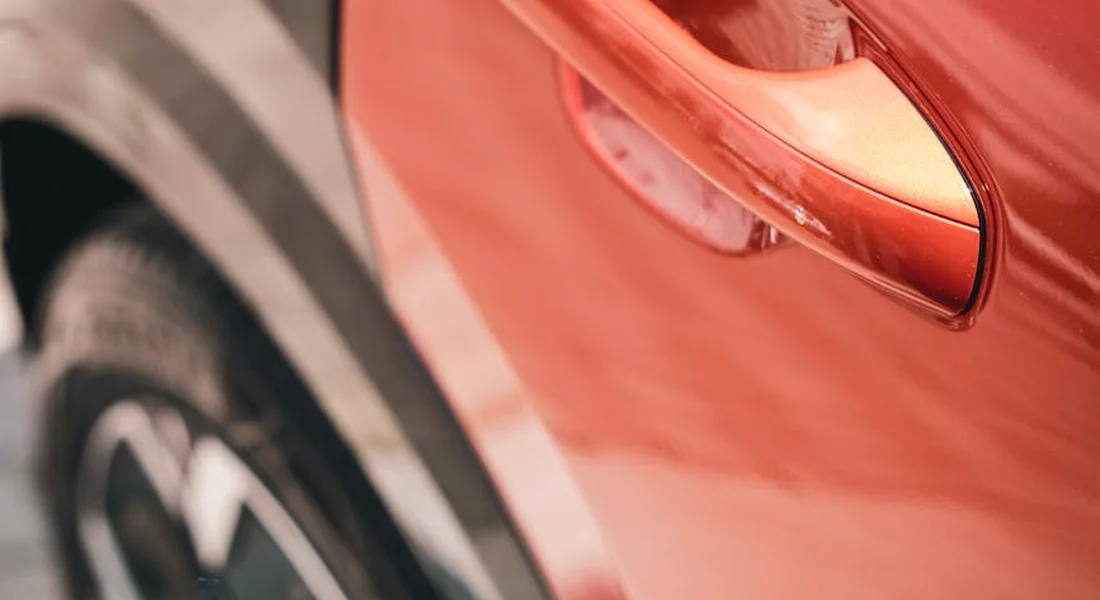 Close-up of a red car door with a visible scratch along the paint