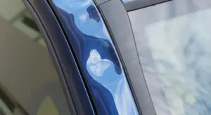 Close-up of a blue car panel near the window, showing the painted surface in preparation