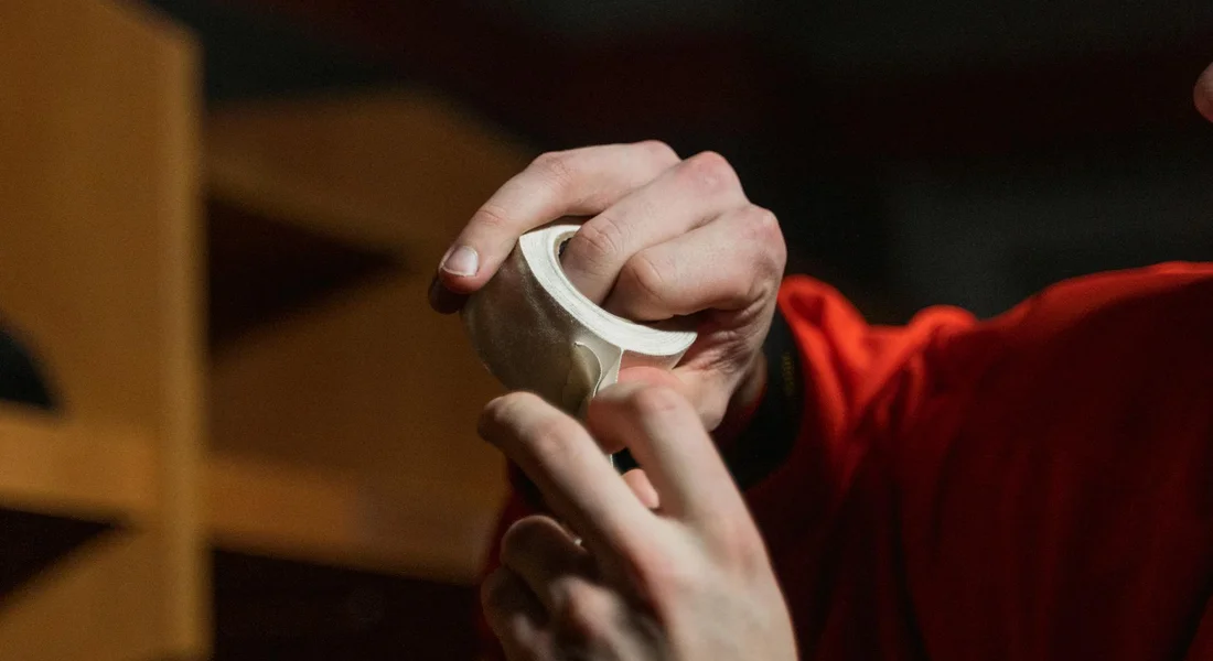 Close-up of hands handling a roll of masking tape in a workshop, illustrating careful tape preparation for car paint protection.