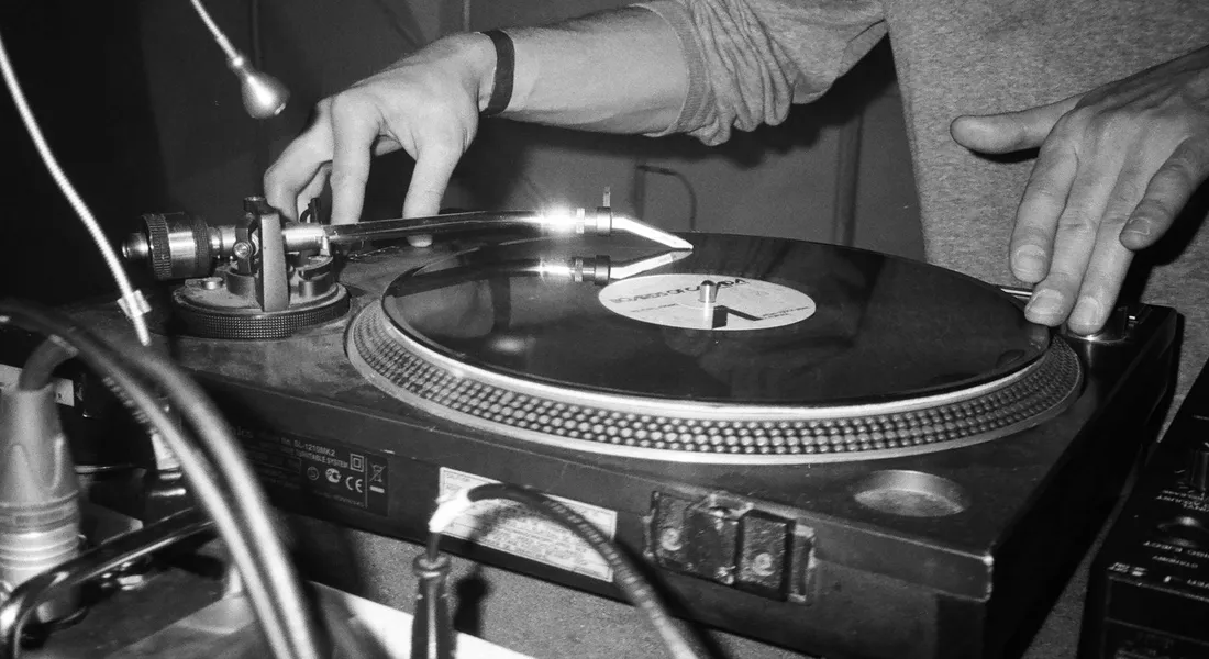 Close-up of a DJ’s hands on a vinyl record spinning on a turntable, black and white.