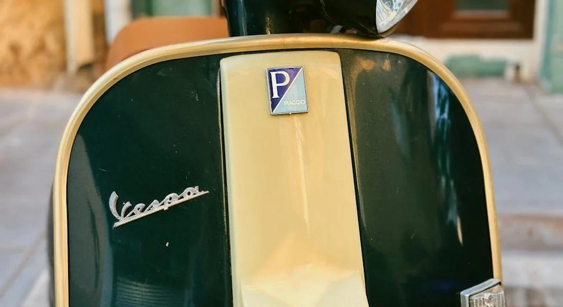 Front view of a vintage two-tone green and beige Vespa scooter with the Vespa emblem visible.