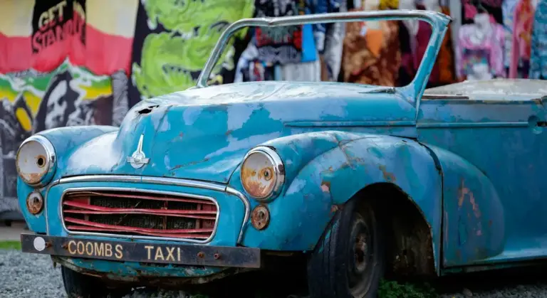 Blue vintage car with chipped and peeling paint parked in front of a colorful graffiti wall