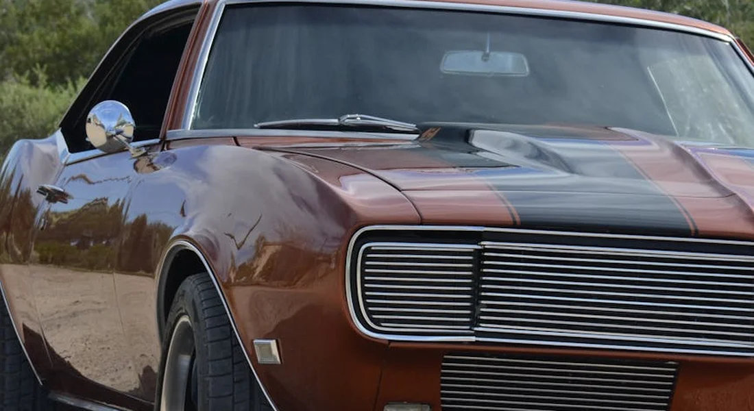 Close-up of a vintage brown car’s front-left section with a chrome grille, showing a glossy paint finish and reflections, illustrating how wax can fill micro-scratches.