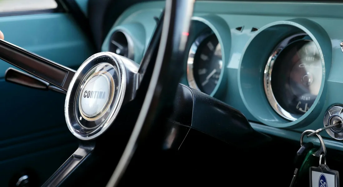 Close-up of a vintage car dashboard with turquoise panels, chrome-rimmed gauges, and a steering wheel.