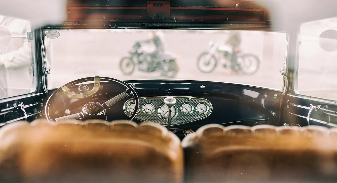 View from the back seat of a vintage car, showing the classic dashboard, steering wheel, and gauges, with brown leather seats