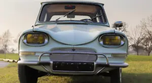 Front view of a vintage silver car with a chrome bumper parked on a grass field