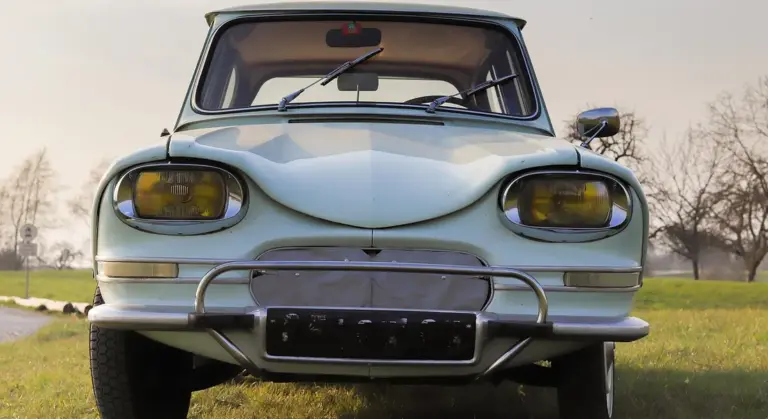Front view of a vintage silver car with a chrome bumper parked on a grass field