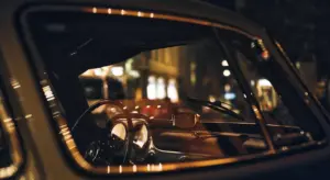 Close-up view of a vintage car's dashboard and steering wheel through a window with reflections at night