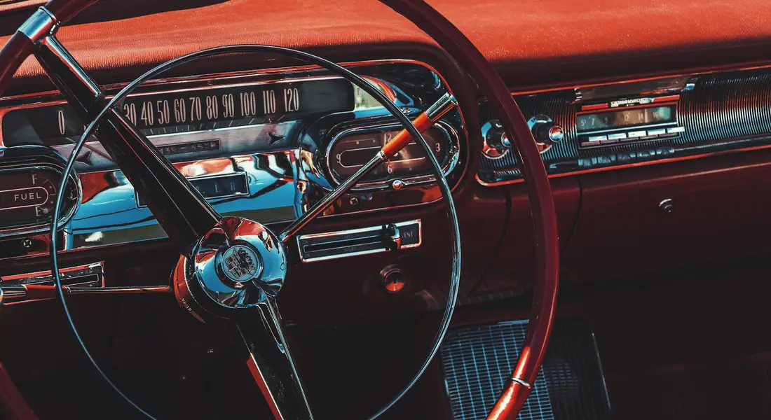 Close-up of a vintage car interior featuring a steering wheel, dashboard, and chrome trim.