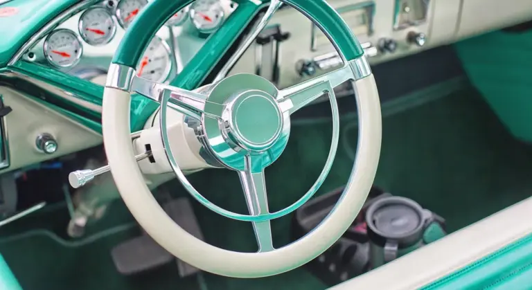 Close-up of a vintage mint-green car interior with a chrome steering wheel and cream-colored rim