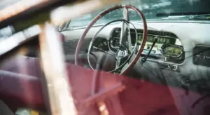 Interior of a vintage car with a wooden steering wheel and dashboard, viewed through the windshield.