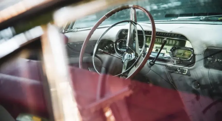 Interior of a vintage car with a wooden steering wheel and dashboard, viewed through the windshield.