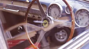 Close-up of a classic car interior with a wooden steering wheel and round analog gauges visible through the dashboard
