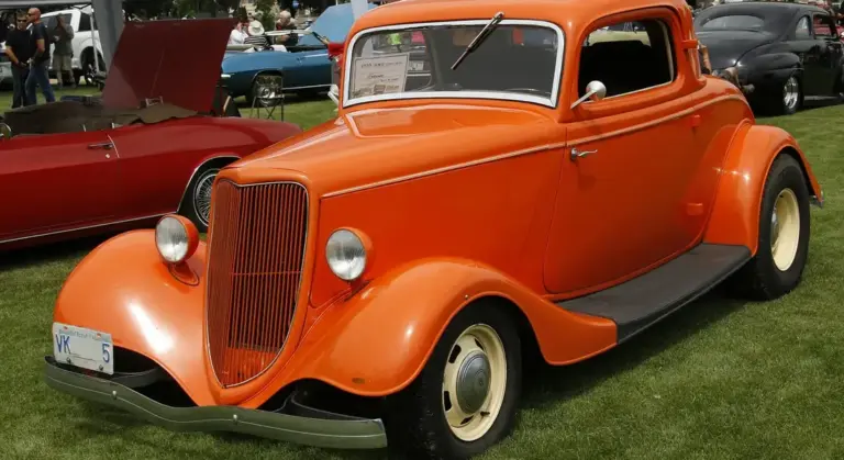 Orange vintage car with gleaming paint at a car show.