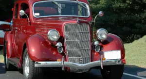 Front view of a vintage red car with a tall chrome grille and polished bumper.