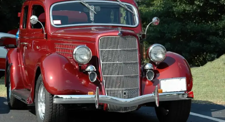 Front view of a vintage red car with a tall chrome grille and polished bumper.