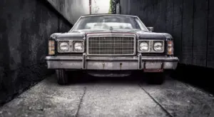 Front view of a vintage car parked in a narrow, shadowy alley with a chrome grille and weathered bumper.