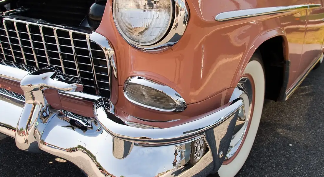 Close-up of a vintage car's chrome bumper and headlight with a peach-colored body